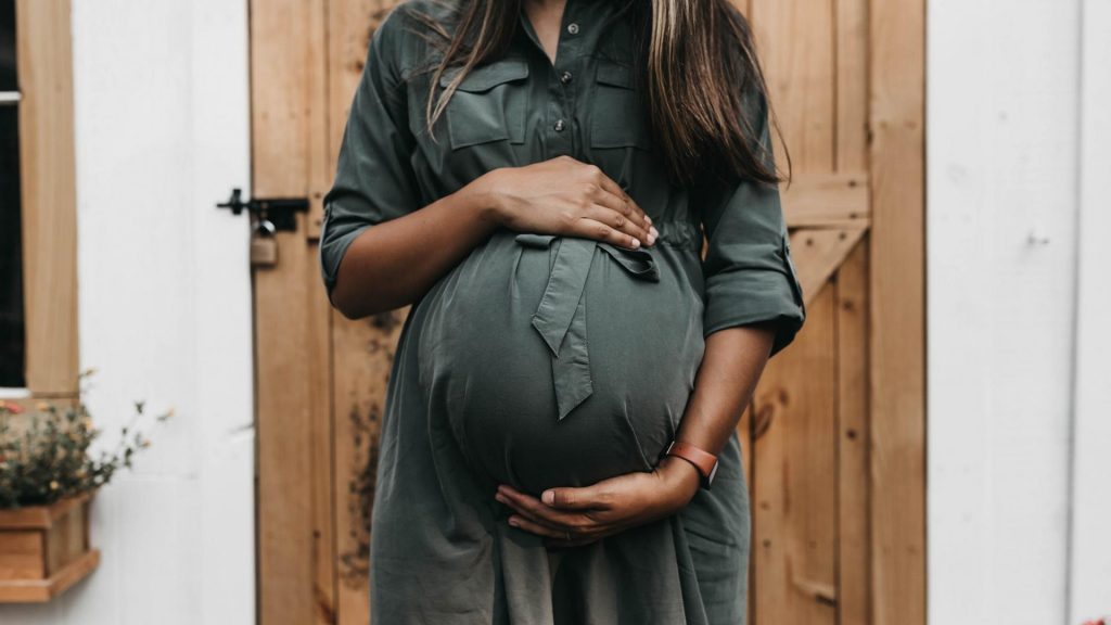 schwangere Frau im dunklen Kleid vor einer Holztür
