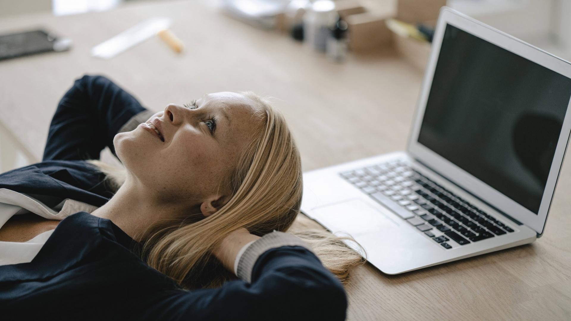 junge Business-Frau lächelt und macht eine Pause am Schreibtisch und legt ihren Kopf auf den Tisch vor dem Laptop