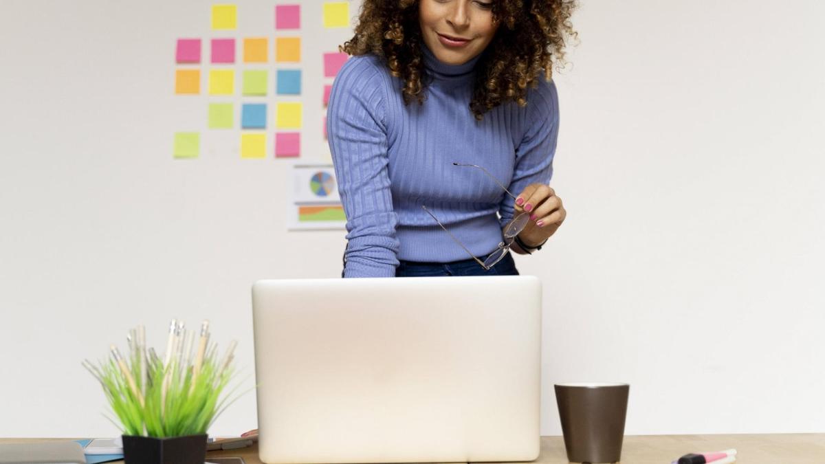 lächelnde junge Frau steht vor ihrem Laptop am Schreibtisch