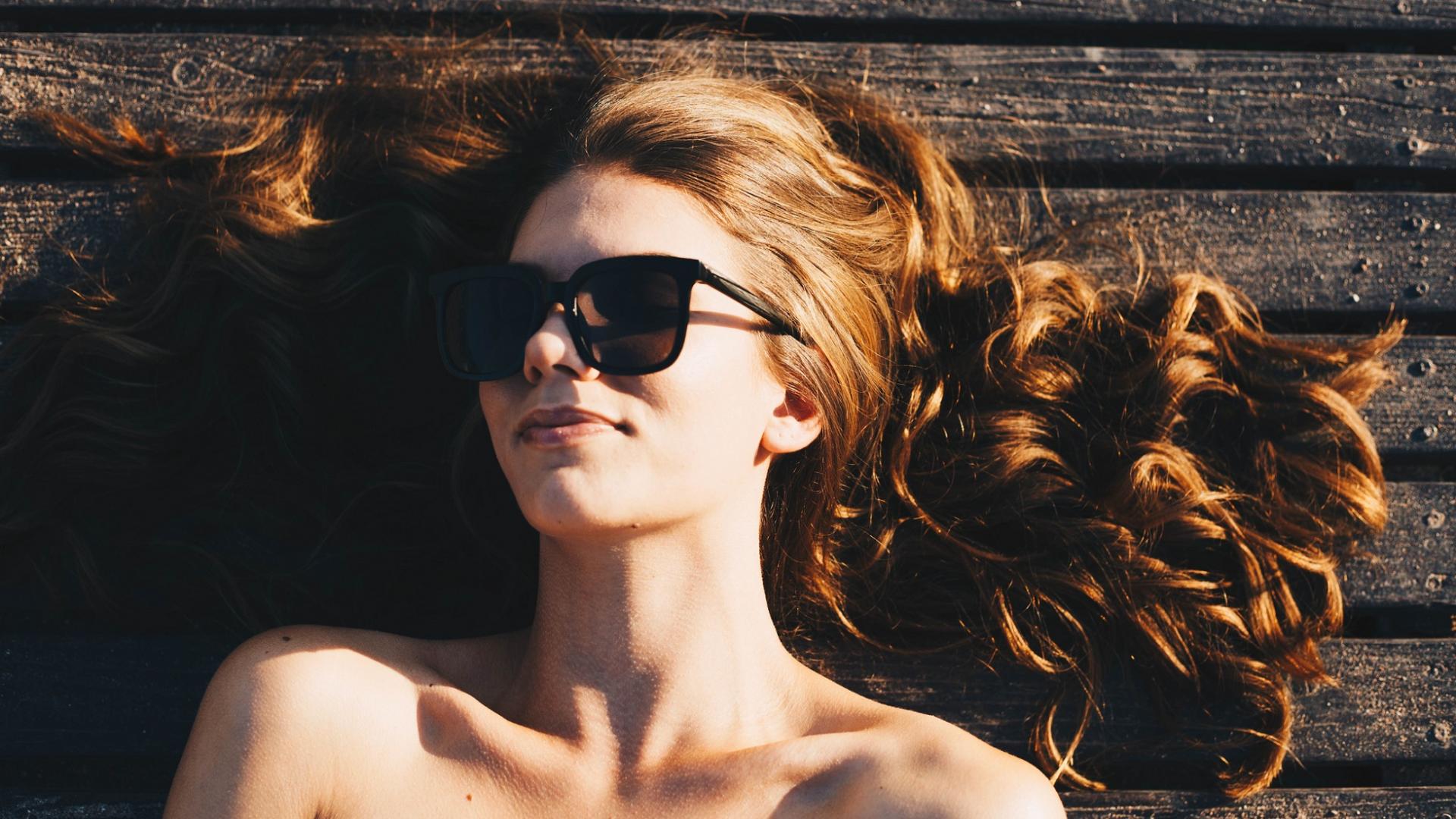 hübsche rothaarige Frau mit Sonnenbrillen liegt auf dem Boden