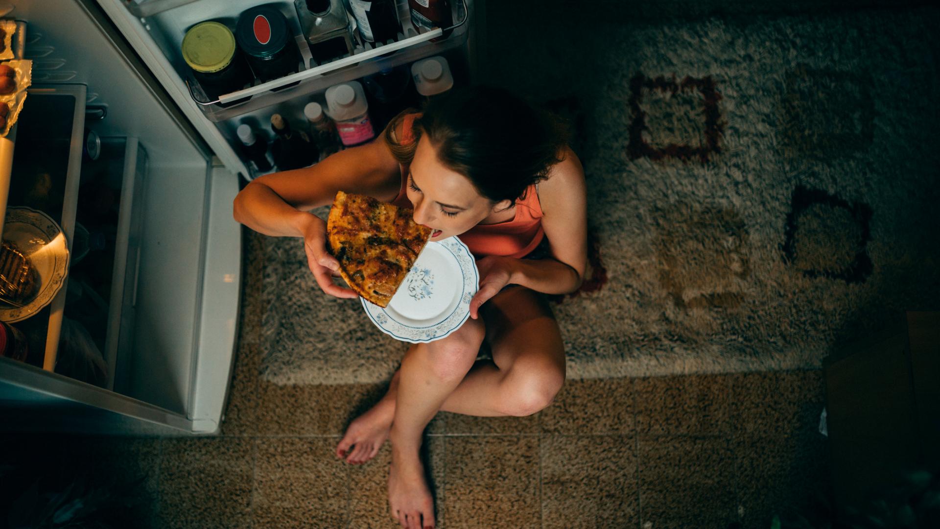 Frau snackt nachts pizza vor kühlschrank