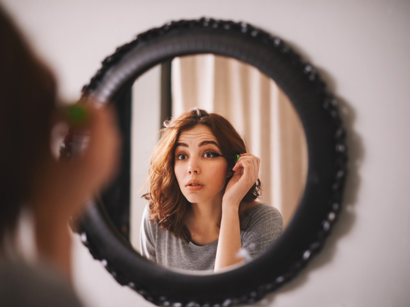 Frau trägt Make Up vor dem Spiegel auf