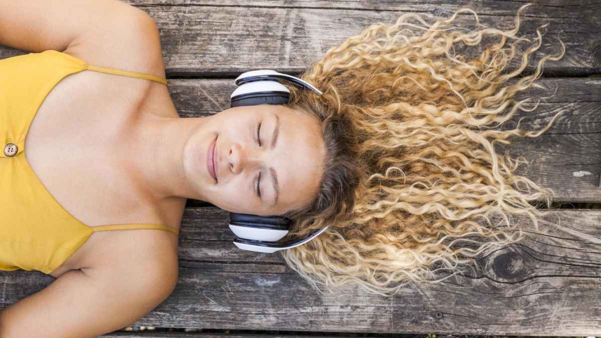 Frau liegt mit geschlossenen augen und lächelt während sie einen Psychologie-Podcast hört