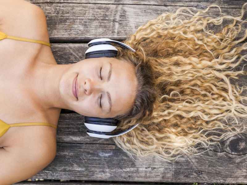 Frau liegt mit geschlossenen augen und lächelt während sie einen Psychologie-Podcast hört