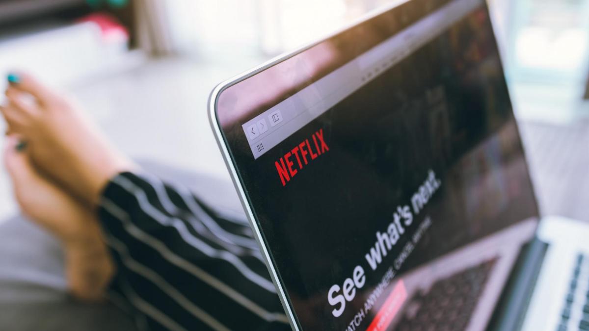 Frau mit lackierten Fingernägeln im Pyjama mit Laptop auf dem Schoß und geöffnetem Netflix-Browser offen