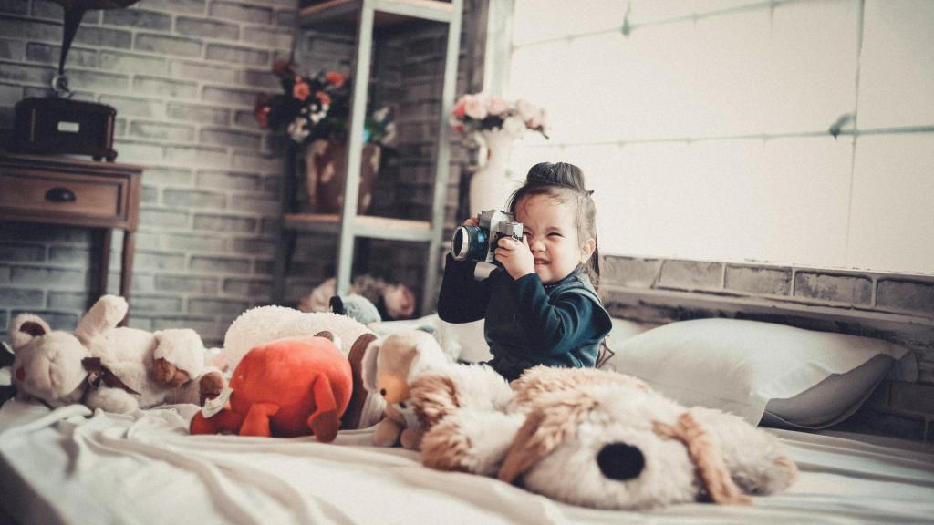 Kind sitzt im Bett mit Kuscheltieren