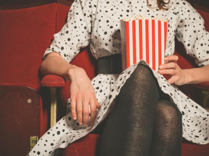Frau sitzt mit Popcorn in der Hand im Kinosaal