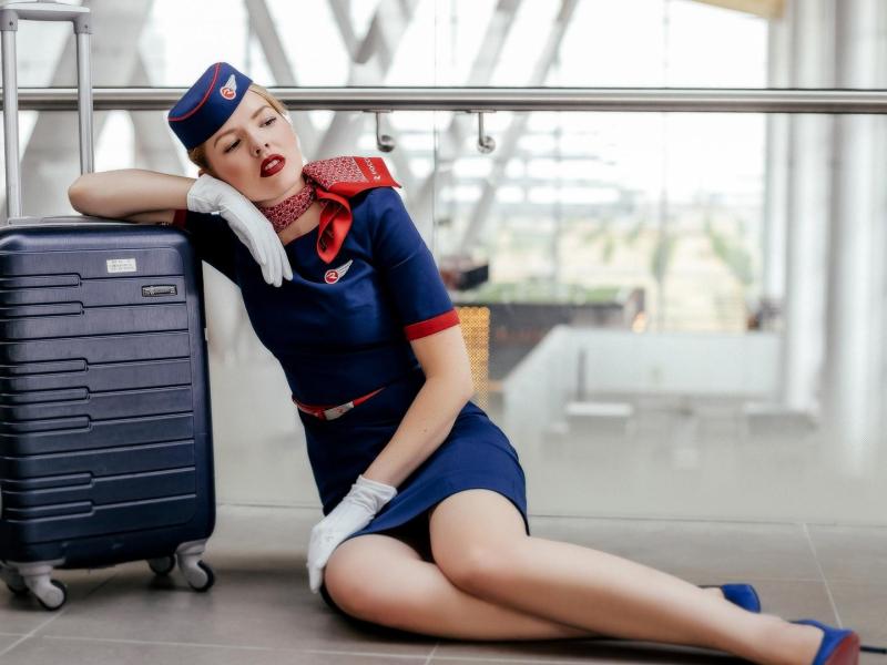 Stewardess sitzt an einen Koffer gelehnt