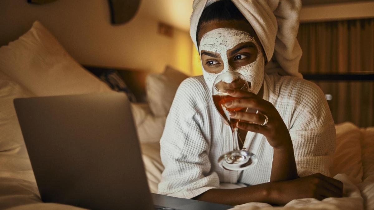 junge Frau entspannt im weißen Bademantel mit Gesichtsmaske schaut Netflix