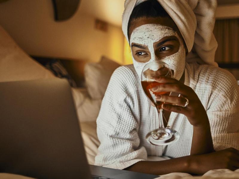 junge Frau entspannt im weißen Bademantel mit Gesichtsmaske schaut Netflix