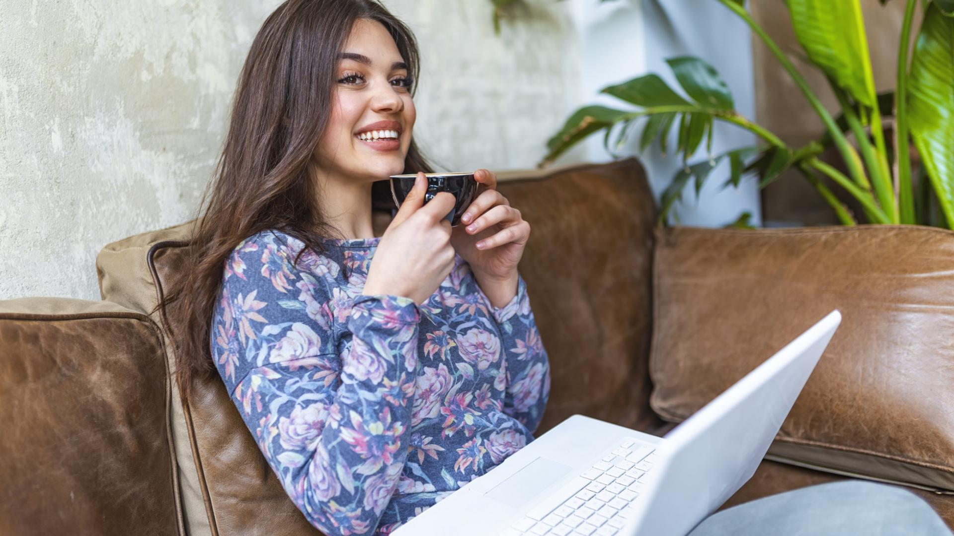 lächelnde Frau macht mit dem Laptop auf dem Schoss eine Pause