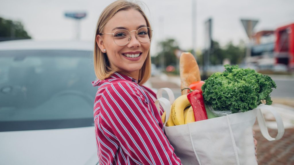 lächelnde Frau mit gestreifter Bluse mit Einkaufsbeutel in der Hand