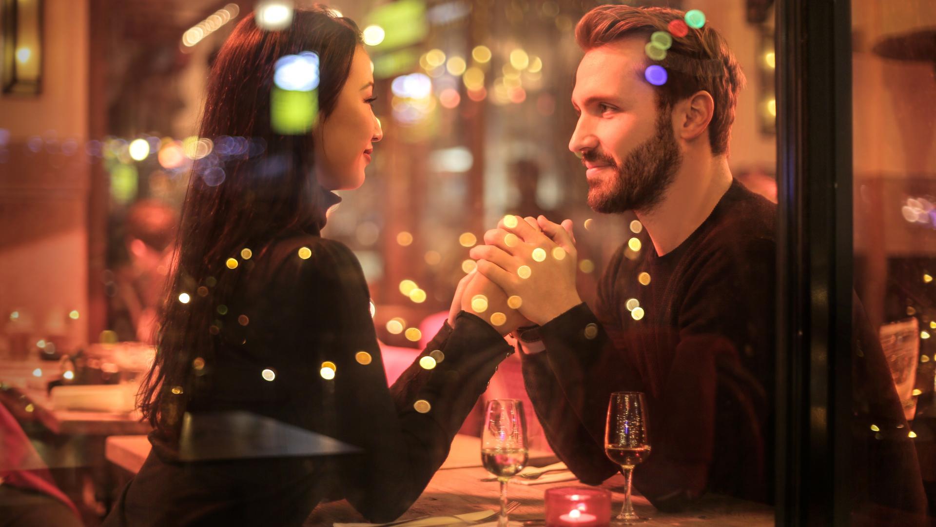 Ein Pärchen sitzt in einem Restaurant bei einem Date hält Händchne