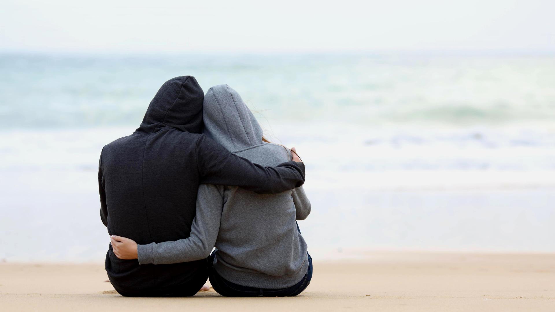 Pärchen sitzt am Strand, einsam und Arm in Arm