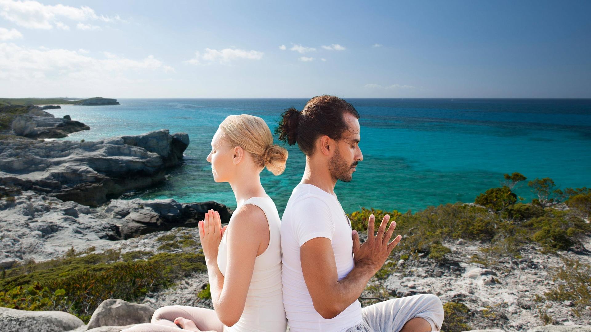 Pärchen sitzt Rücken an Rücken beim Partneryoga und meditiert