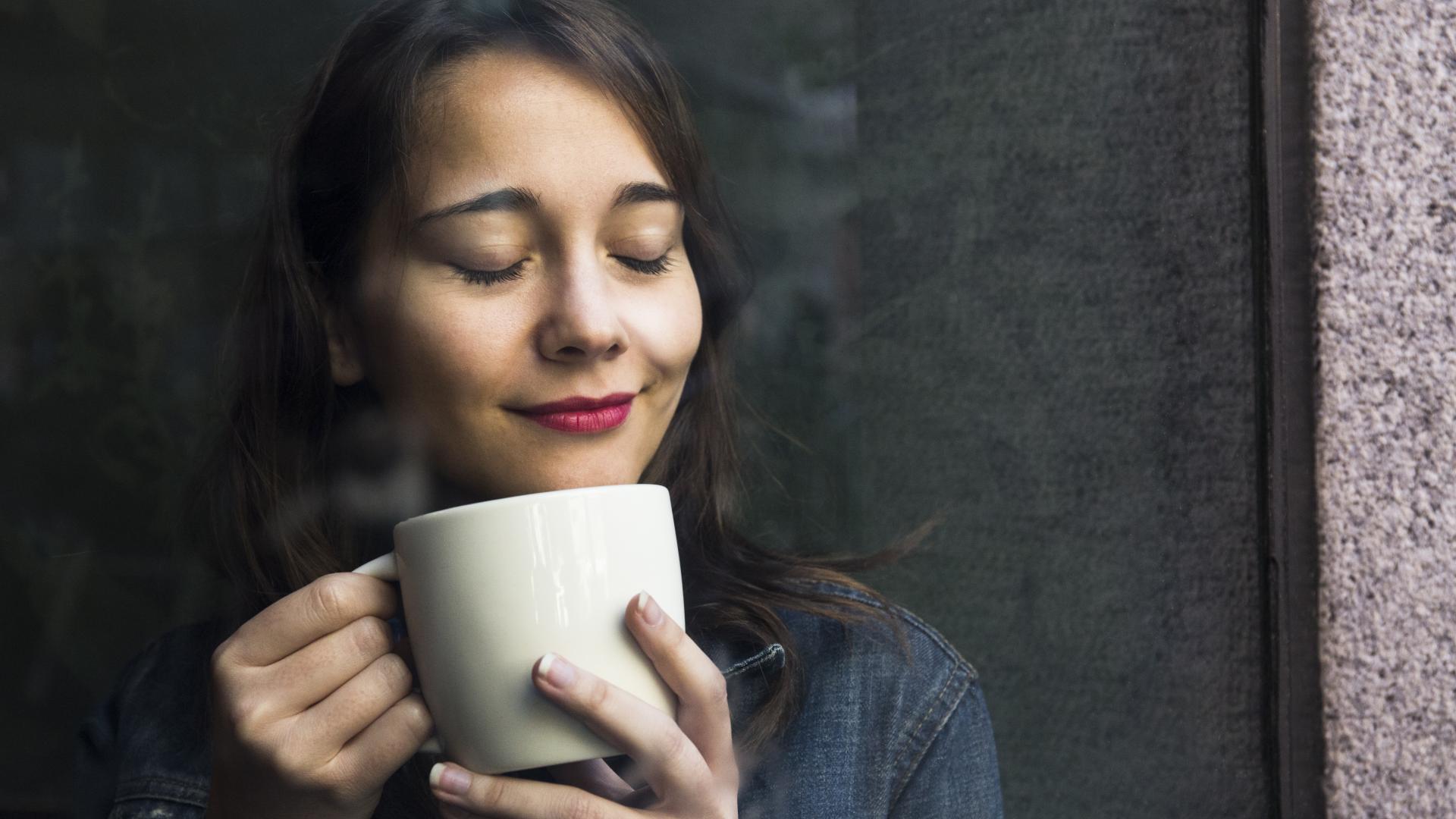 Frau lächelt mit geschlossenen Augen und ihrer Tasse Alternativen Kaffee in der Hand