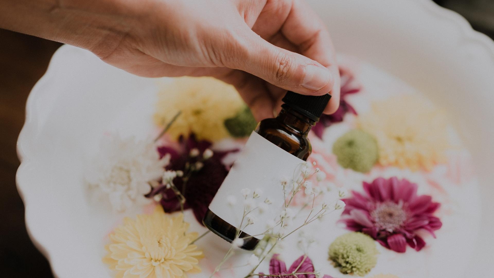 Hand hält Öl vor einer Schüssel mit Blumen