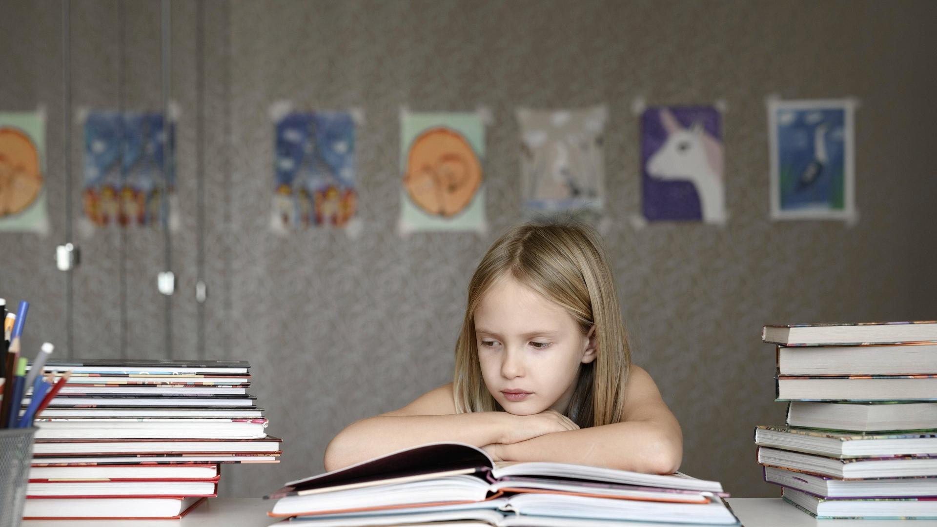 Mädchen sitzt genervt über Schulbüchern