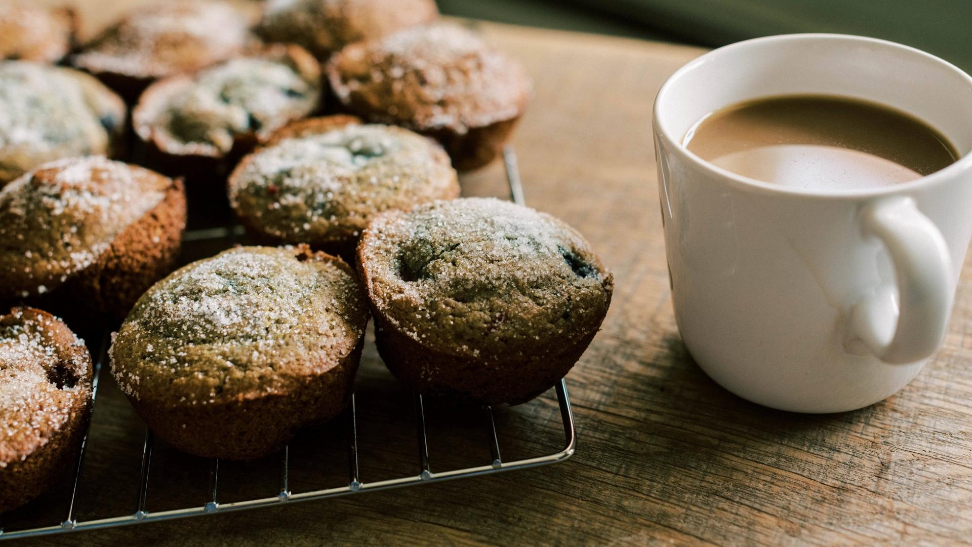 frisch gebackene Muffins mit Puderzucker auf Backgitter neben Kaffeetasse