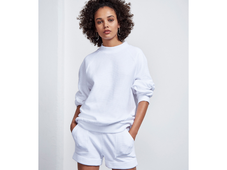 Frau mit Afrolocken und weißem Pullover sowie Shorts