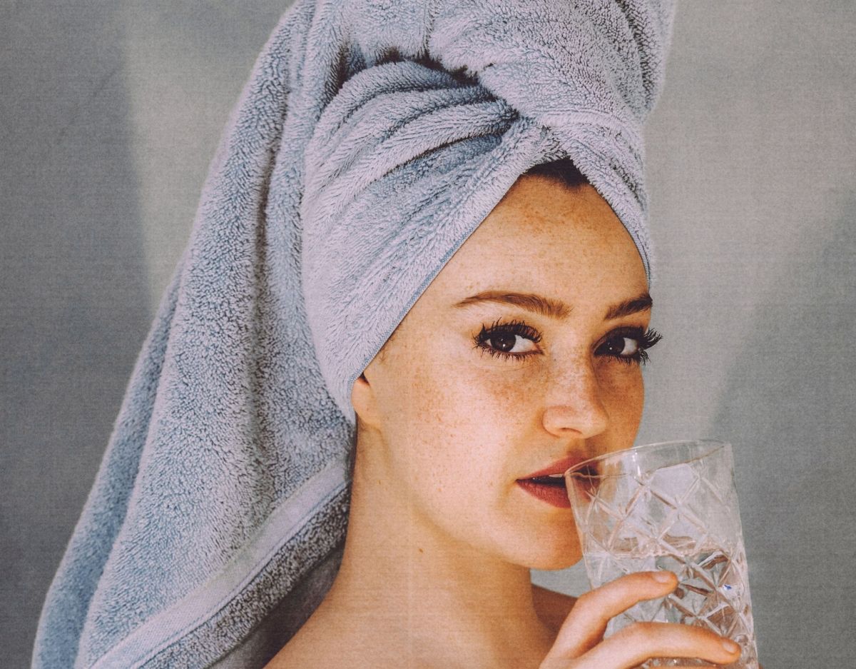 Frau mit Handtuch auf dem Kopf und Wasserglas in der Hand