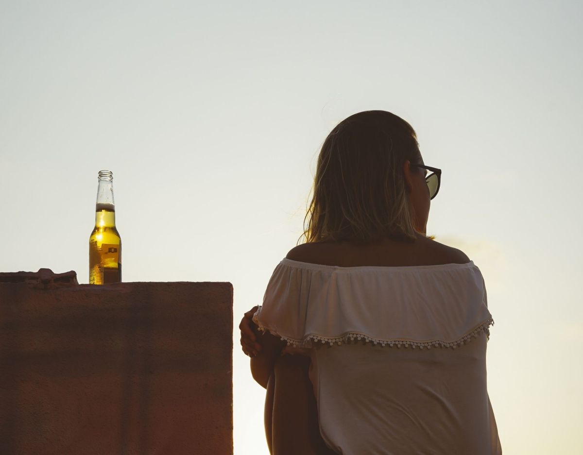 Frau sitzt mit Bier auf Dach