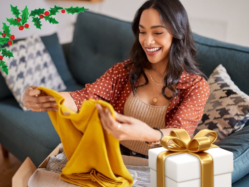 Eine Frau packt ein gelbes Kleidungsstück aus einem Paket aus. Daneben steht ein Geschenk.