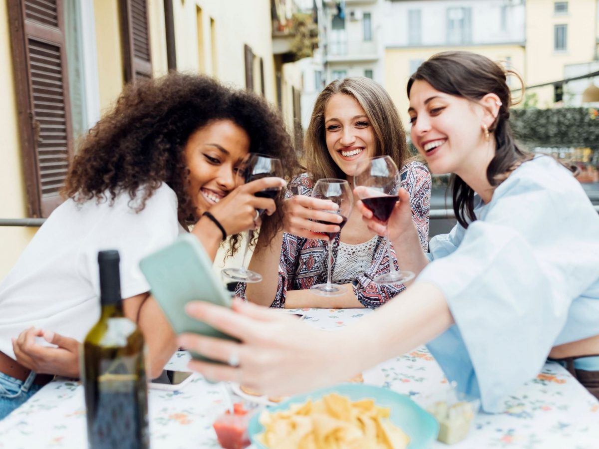 Frauen stoßen an mit Wein und machen ein Selfie