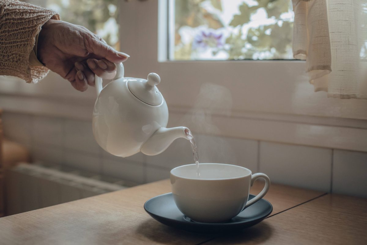 Hand gießt Tee in Tasse ein