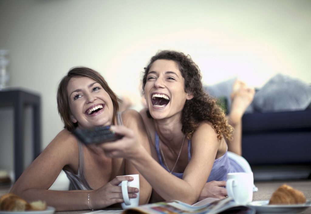 Frauen halten Fernbedienung fest und lachen.