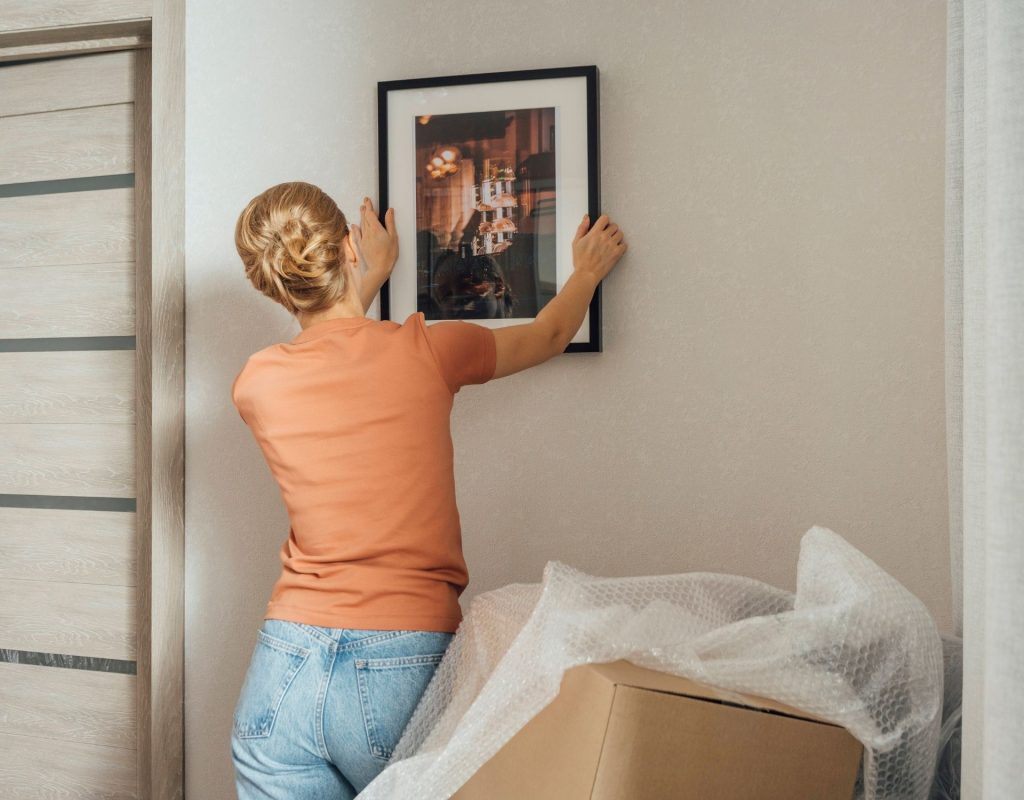 Frau hängt Bild auf um Wohnung minimalistisch einzurichten