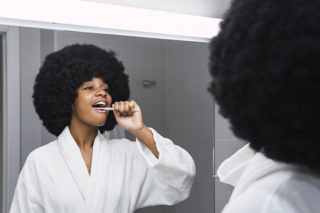 Frau putzt sich Zähne vor Spiegel verschlafen