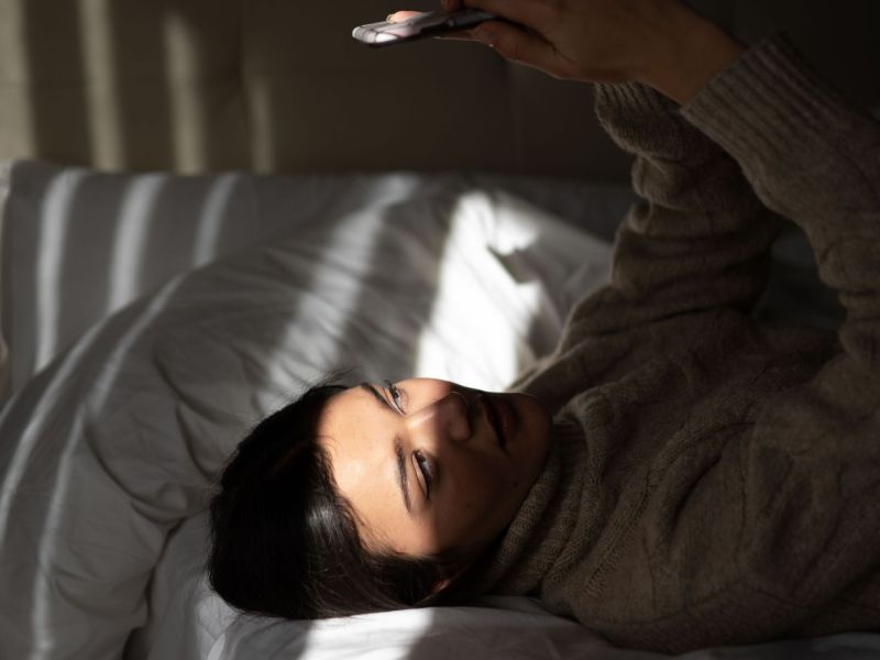Frau liegt mit Handy auf dem Bett