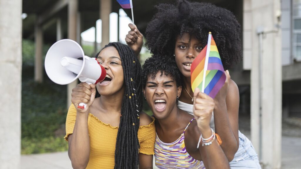 Drei Frauen mit Regenbogenflagge und Megafon