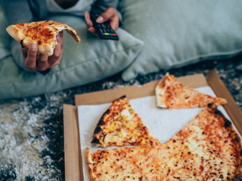 Junge Frau isst Pizza vor dem Fernseher