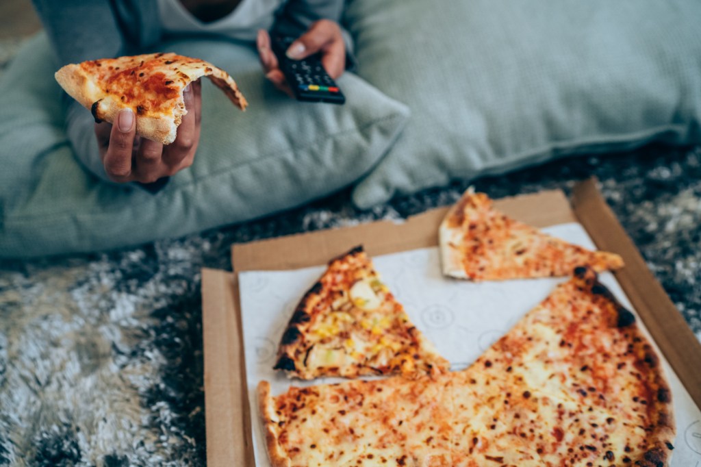 Junge Frau isst Pizza vor dem Fernseher