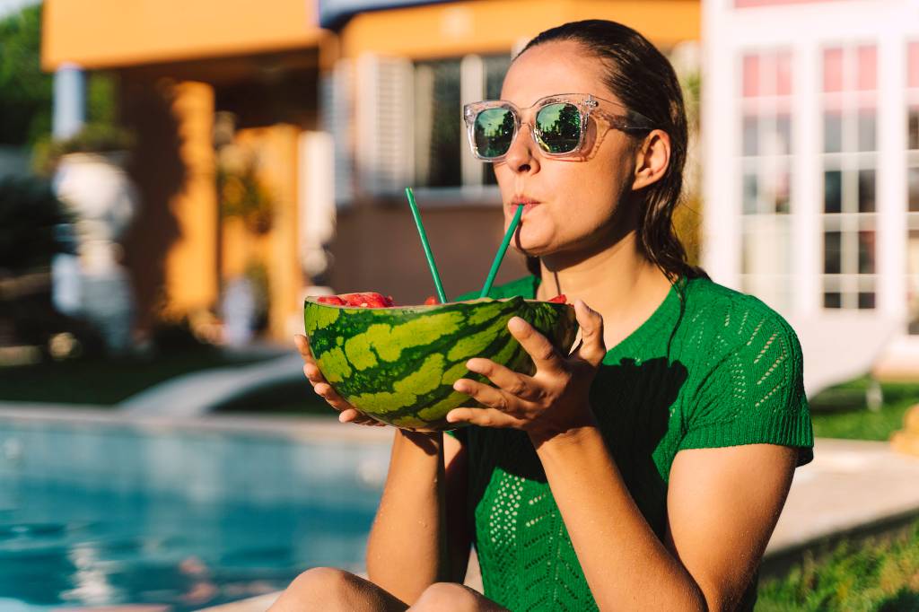 Frau trinkt am Pool aus Wassermelone