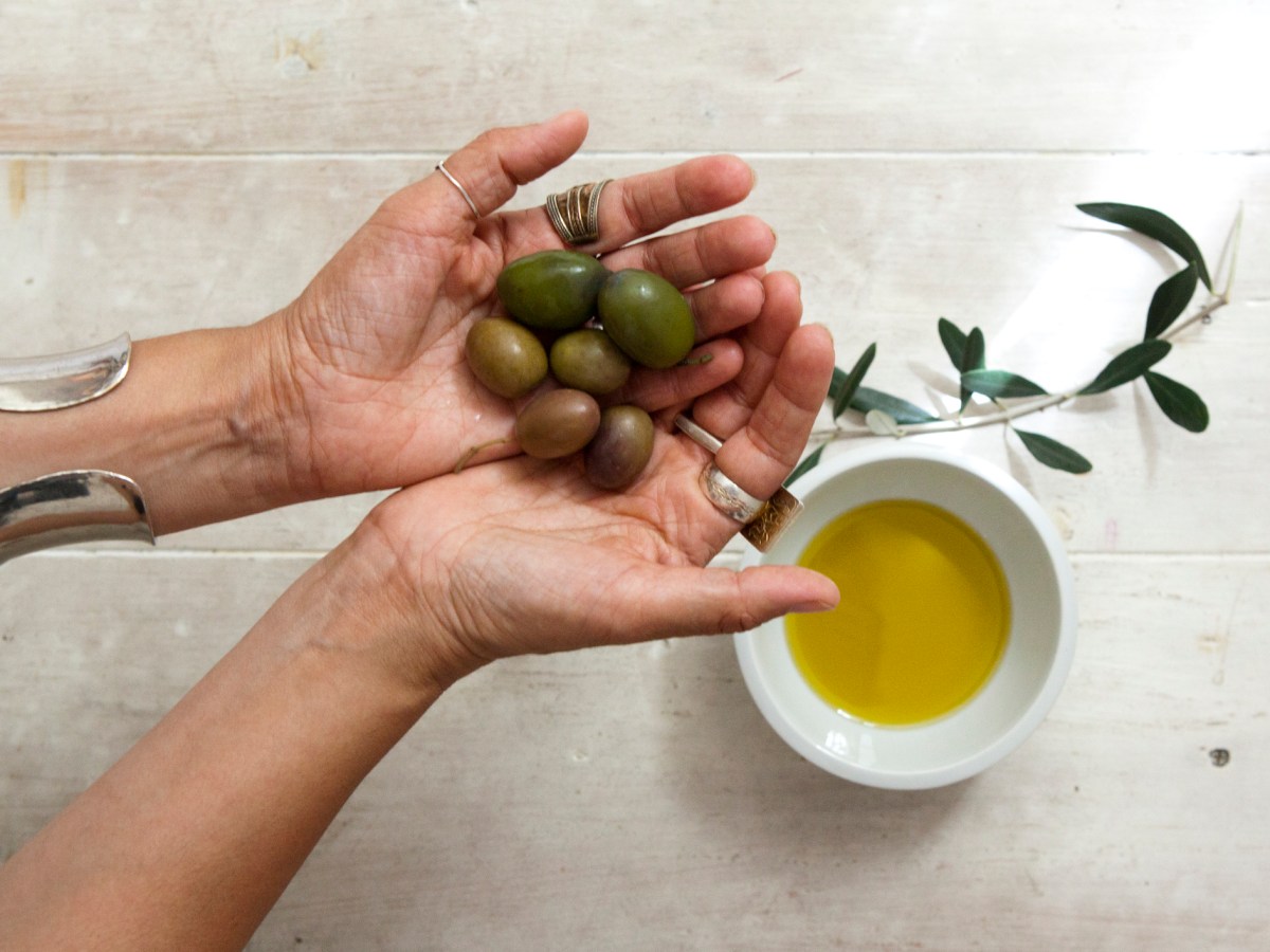 Frau hält Oliven neben Schale Olivenöl