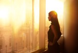 Eine Frau steht im Büro vor dem Fenster. Es ist Sonnenuntergangsstimmung.