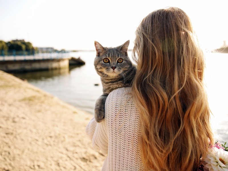 Frau hält Katze am Strand auf dem Arm.