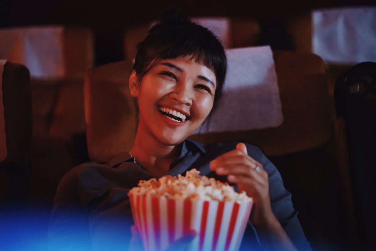 Frau sitzt lachend mit Popcorn im Kino