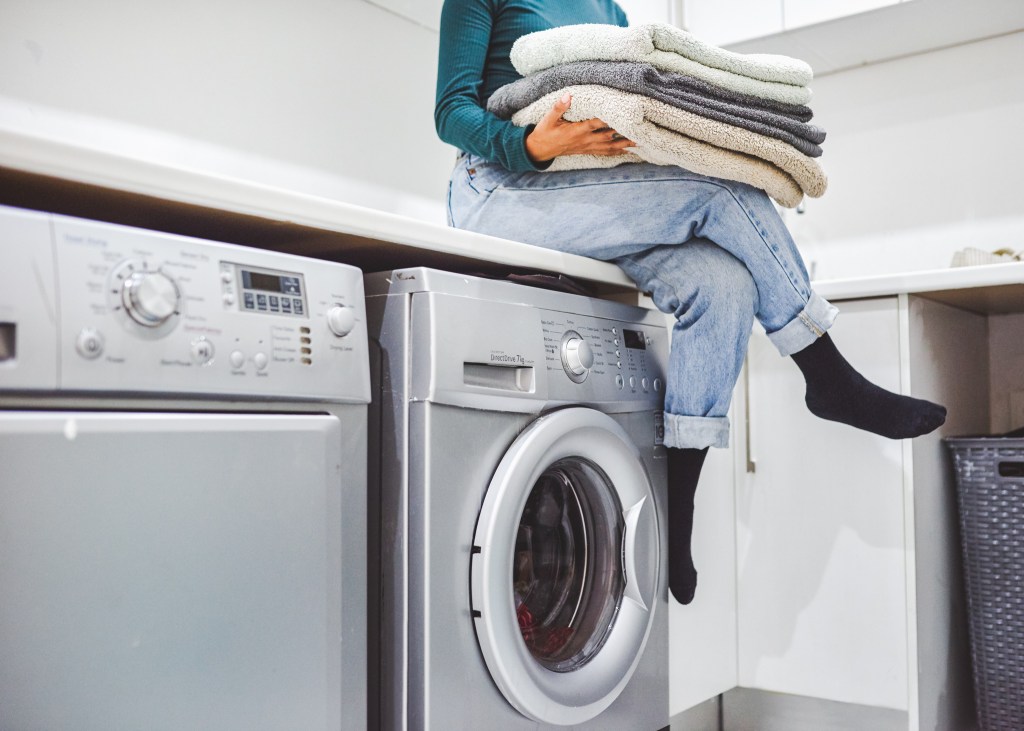 Frau sitzt mit Handtüchern auf Waschmaschine