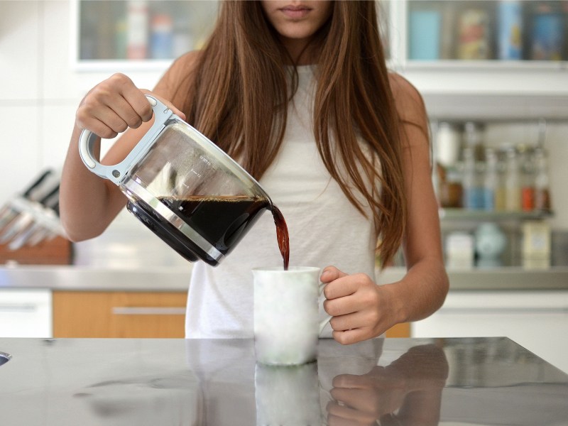 Junge Frau gießt Kaffee in eine Tasse.