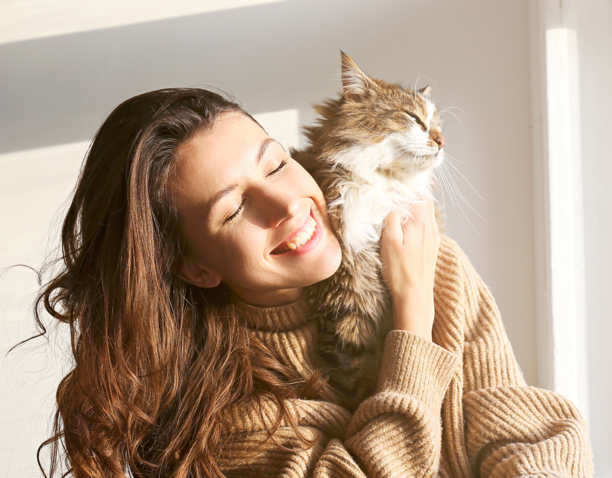 Frau hat Katze auf dem Arm und lacht.