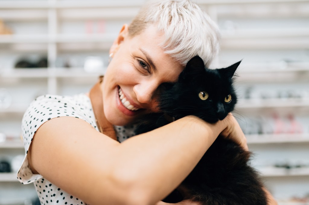 Frau hält schwarze Katze im Arm.