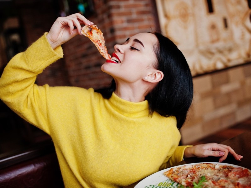 Frau im gelben Pullover isst Pizza