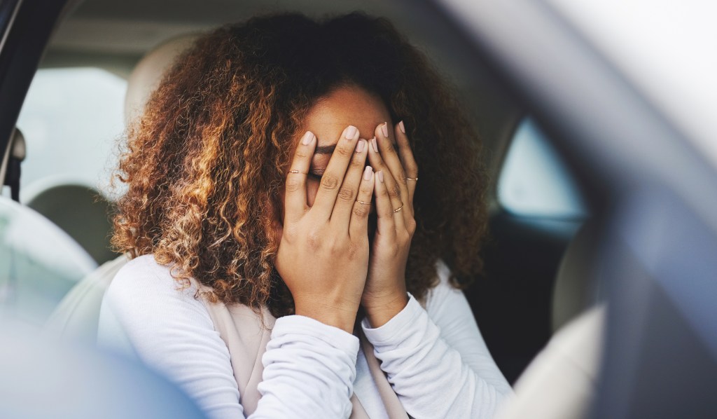 Frau im Auto hält sich die Augen zu.