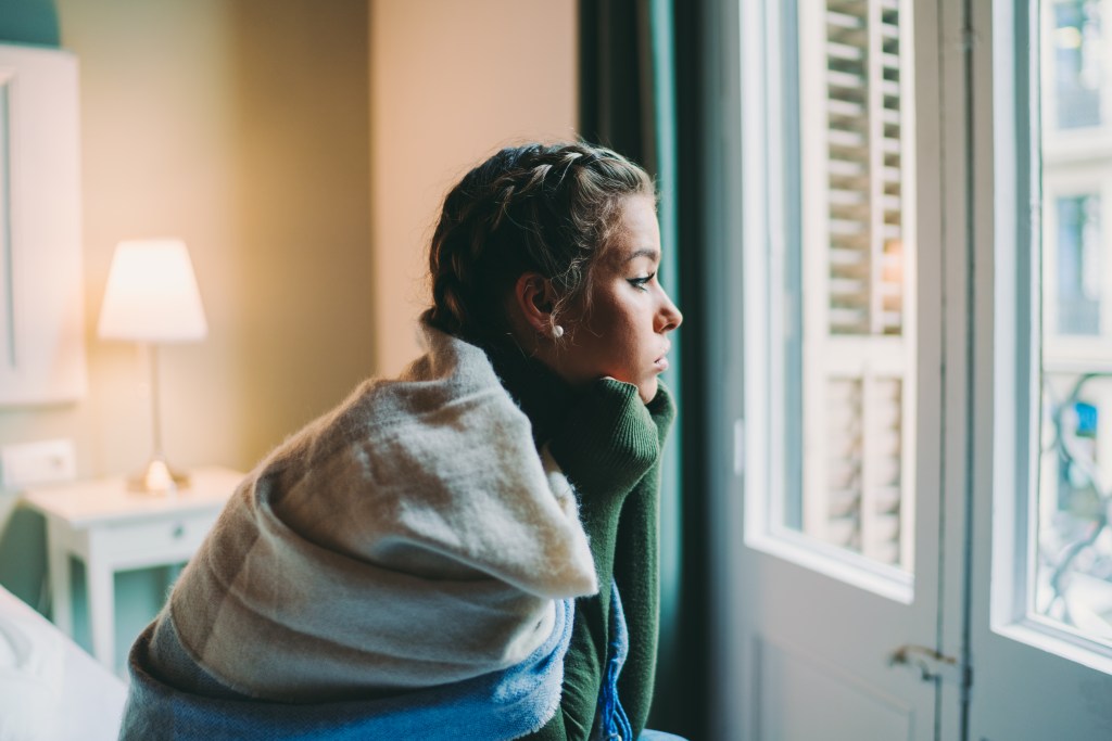 Frau sitzt auf dem Bett und schaut aus dem Fenster.