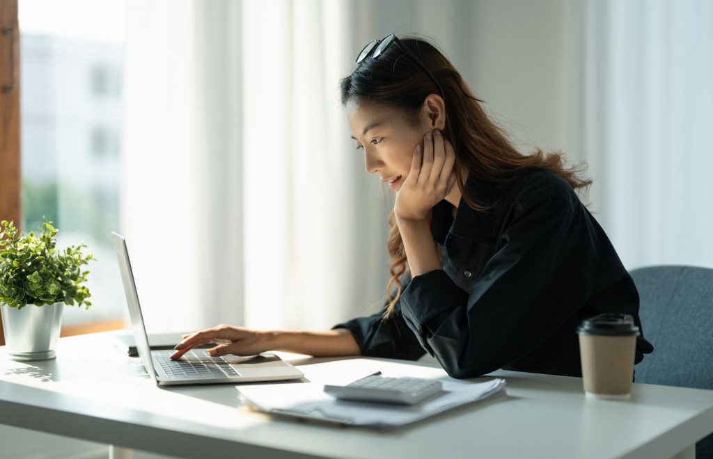 Frau sitzt am Laptop und rechnet etwas durch