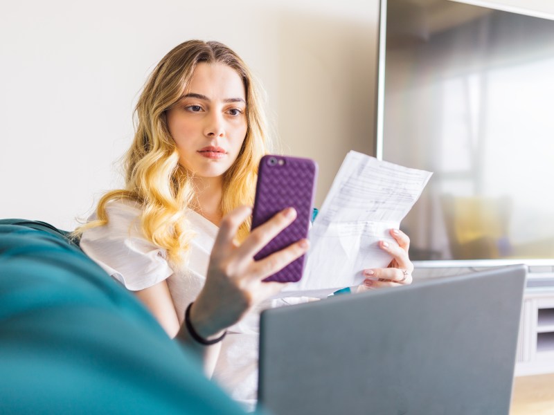 Frau hält Handy und Unterlagen in der Hand.